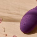 Succionador de clítoris morado sobre una superficie de madera rodeado de pétalos rosas